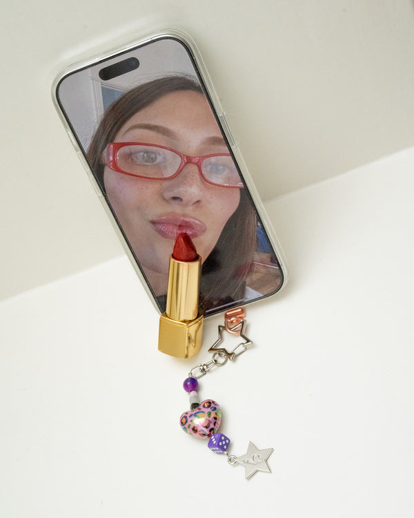 Phone mirror selfie with a purple heart and star beaded charm, dice bead, and a pink lipstick – barneys favorite charm
