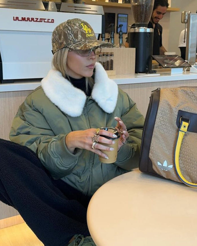 Woman in a green jacket at a coffee shop counter wearing the camo IC daddy cap