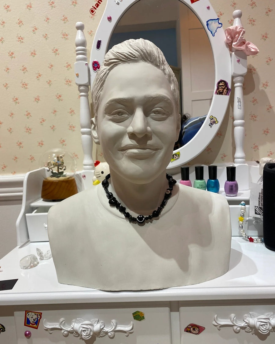 Sculpted white bust at a vanity wearing the smoker necklace, an all-black beaded charm necklace