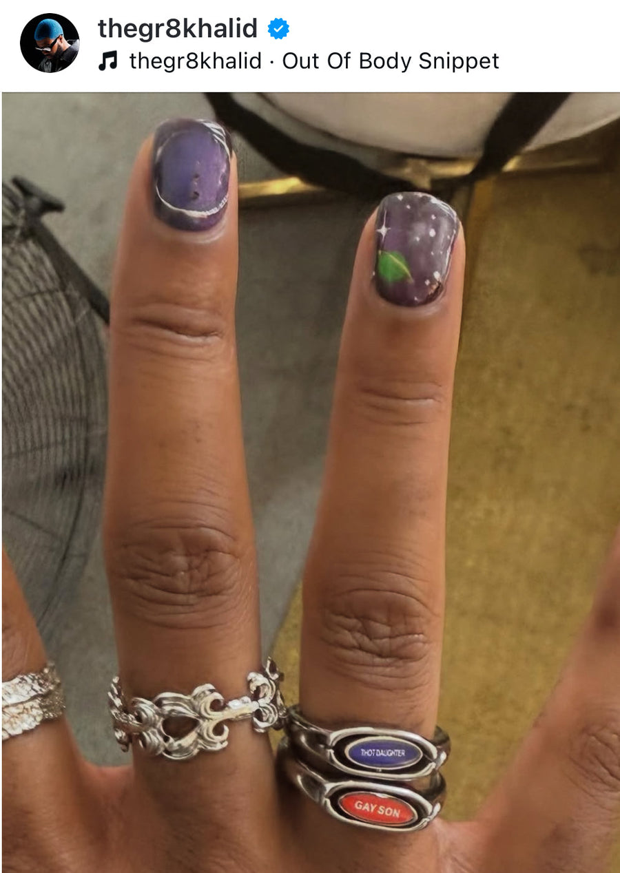 Social media screenshot of a hand with painted nails wearing stacked silver rings including the red pill or blue pill ring
