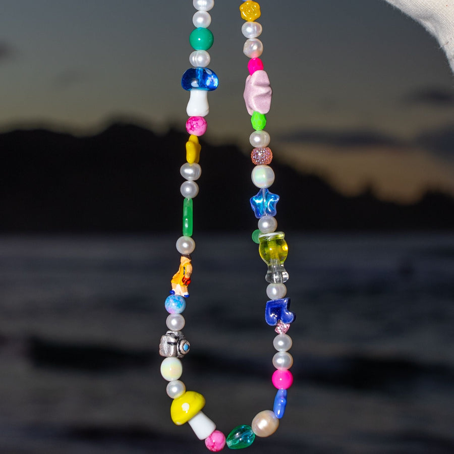 Custom beaded necklace with mushroom, star, heart and smiley glass beads against a sunset over water