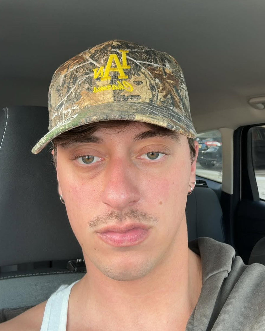 Man taking a selfie in a car wearing the camo IC daddy cap with yellow logo