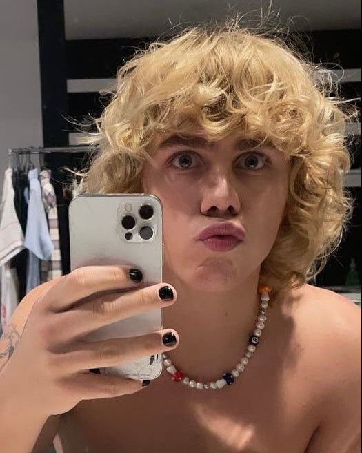 Curly-haired man taking a mirror selfie wearing a pearl necklace with mushroom and 8-ball beads