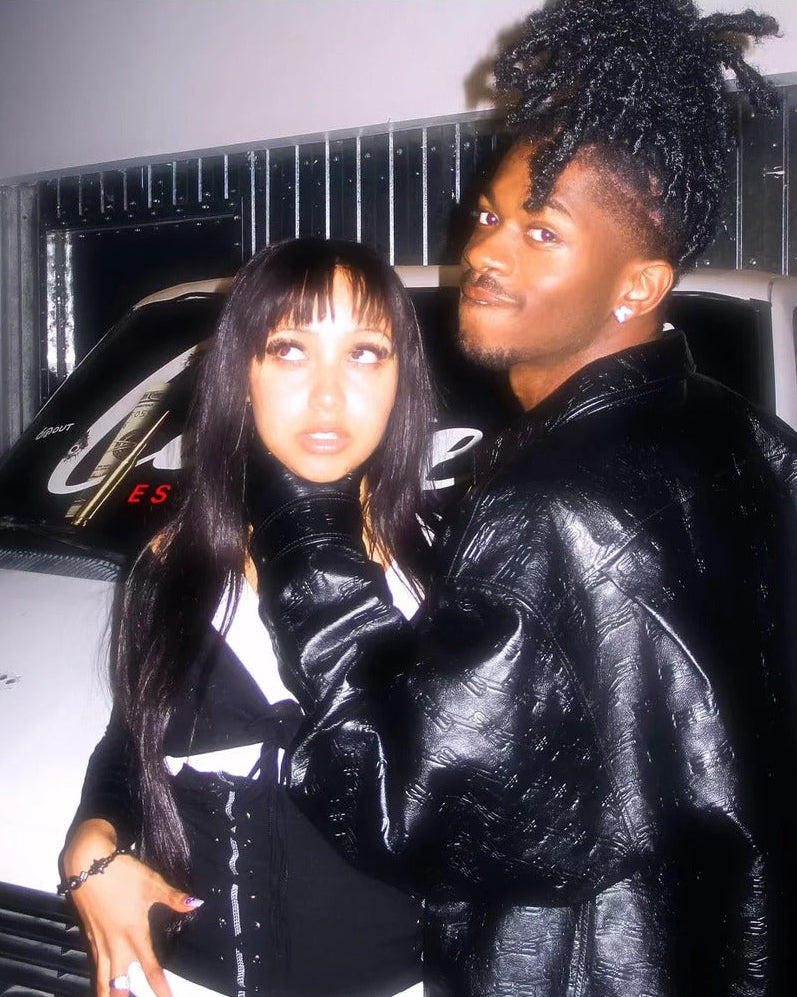 Couple in black leather jackets posing by a car at night, wearing black beaded bracelets