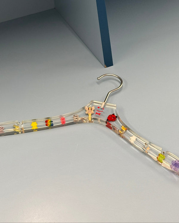 Clear acrylic hanger embedded with colorful Ian Charms beads on a gray floor – Staff x Ian Charms Hung Up on U hanger