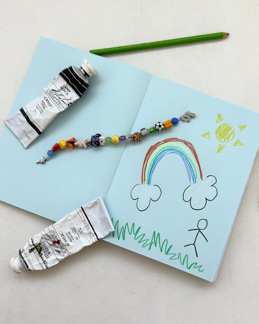 The get a hobby beaded bracelet on a sketchbook with paint tubes, a pencil and a rainbow doodle