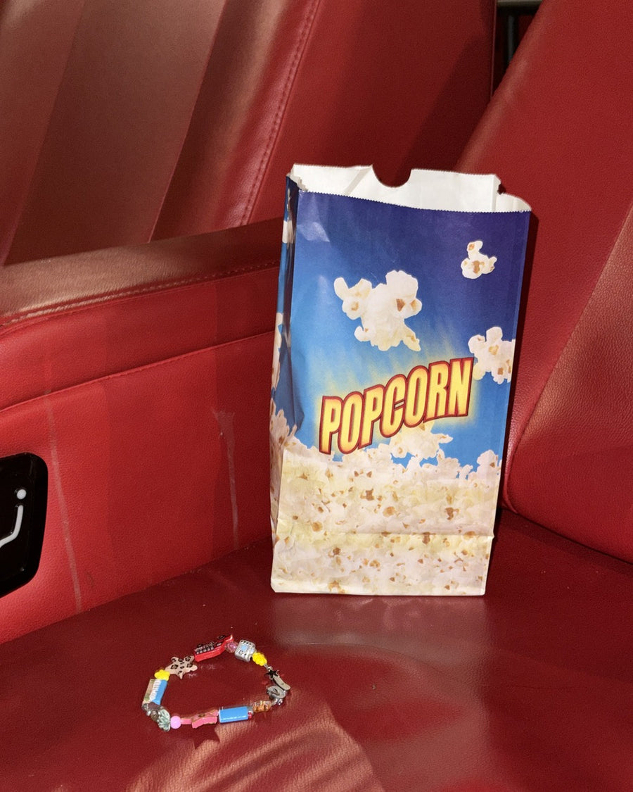 The LA bracelet on a red movie theater seat beside a striped popcorn bag