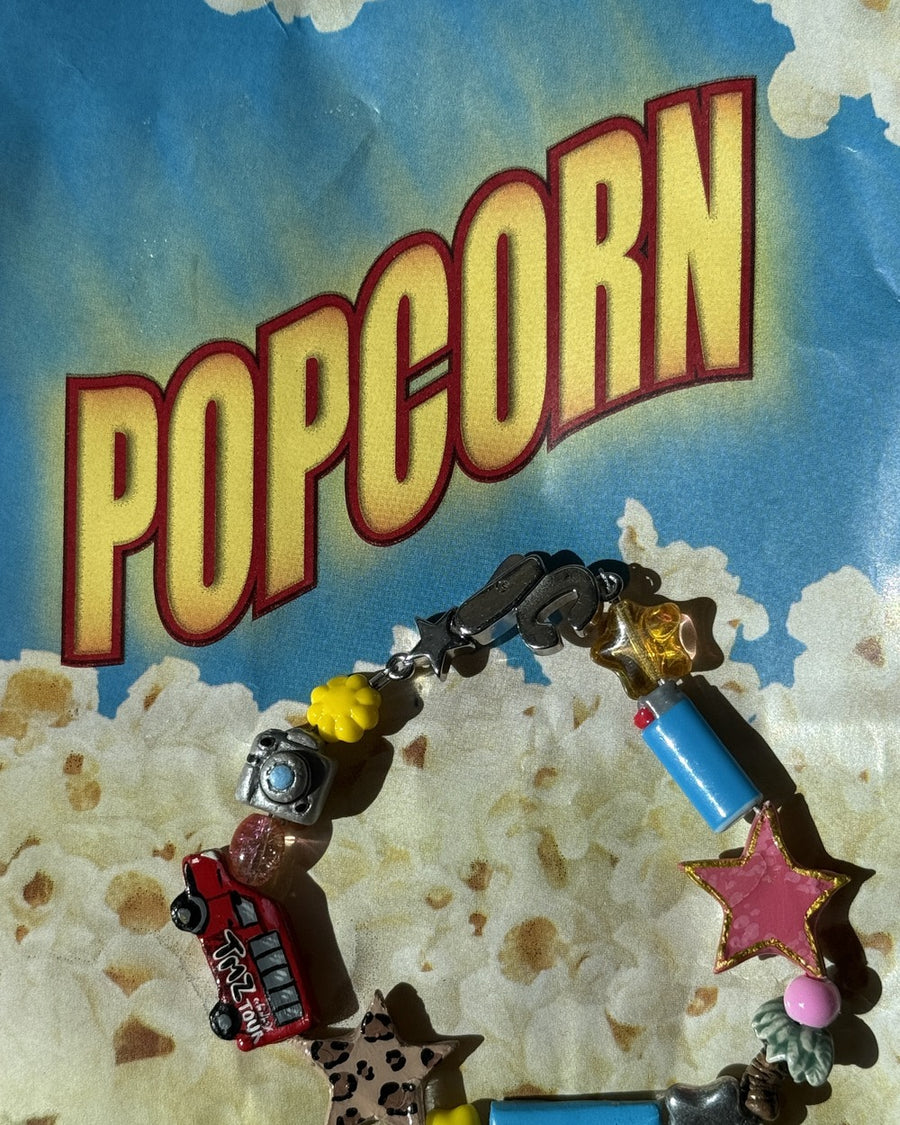 Close-up of the LA bracelet's red bus and pink star beads against a vintage popcorn poster