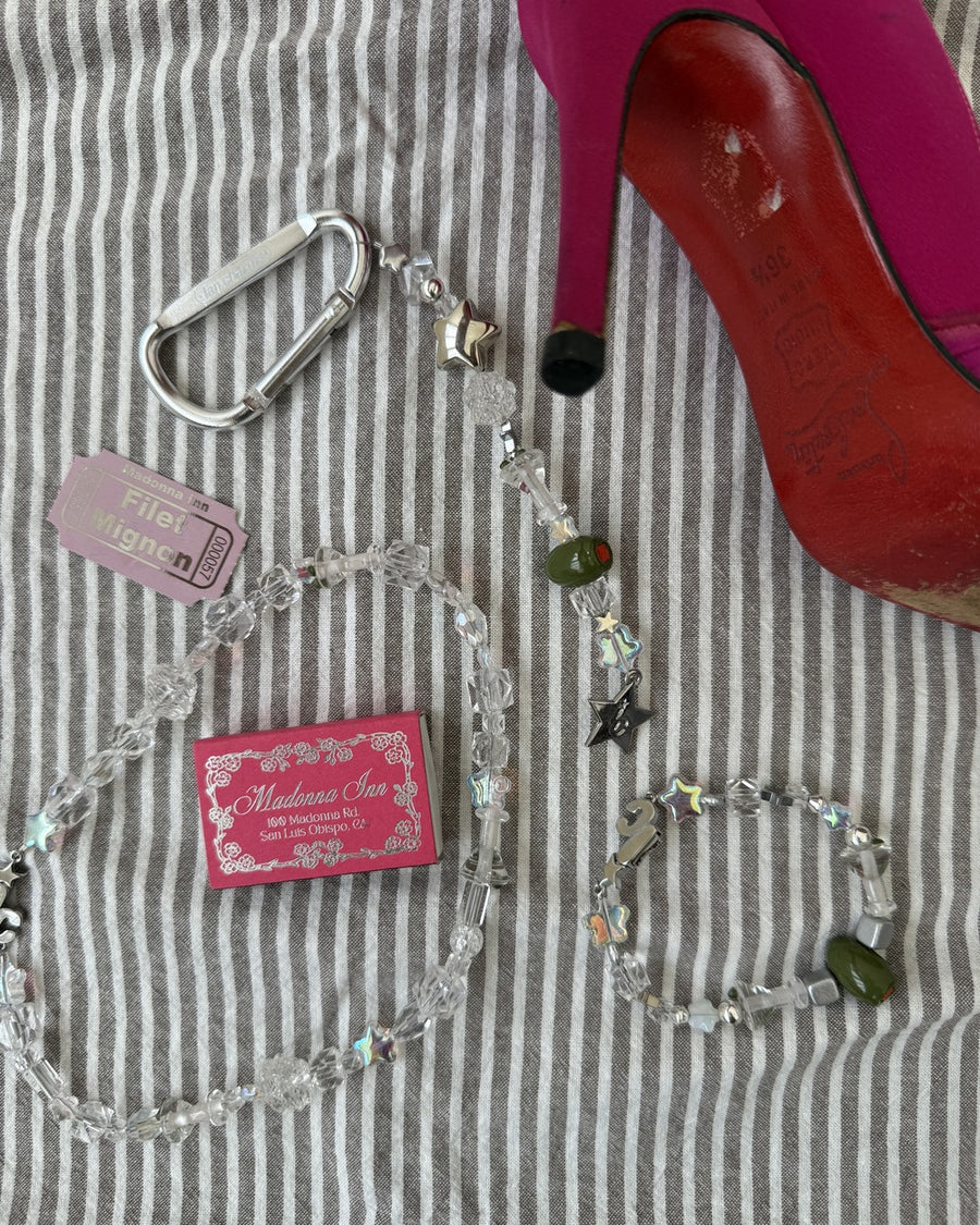 The usual clear bead bracelet and keychain on striped fabric beside a pink heel and matchbox