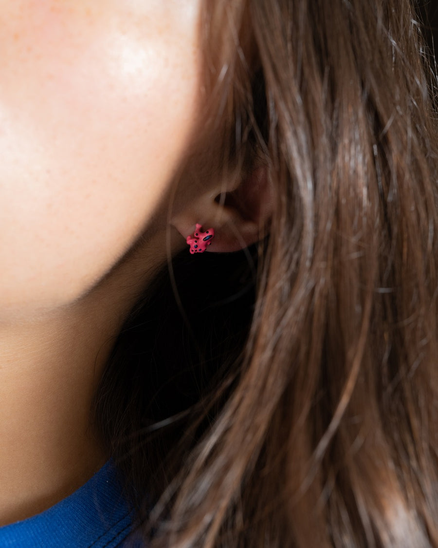 Close-up of a pink frog stud earring peeking from behind long brown hair