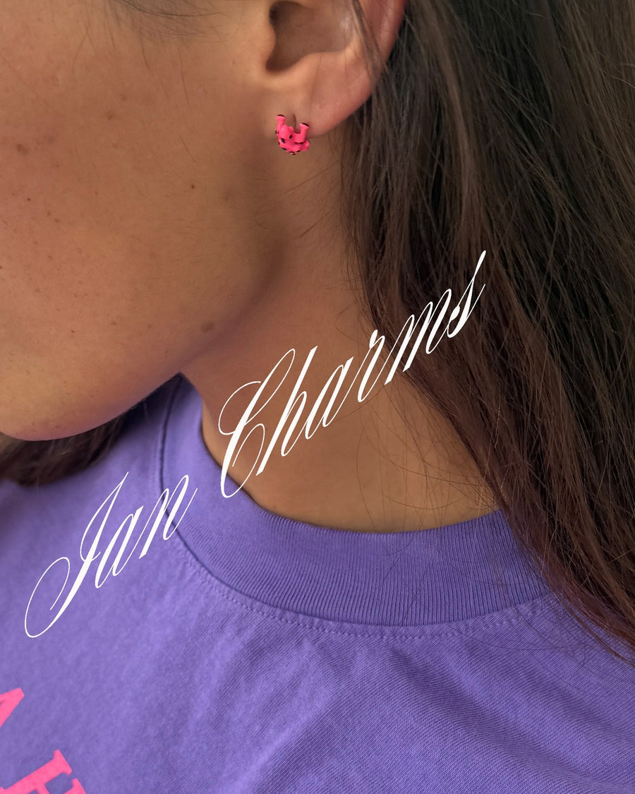 Close-up of a pink frog stud on a woman in a purple tee with Ian Charms script overlay