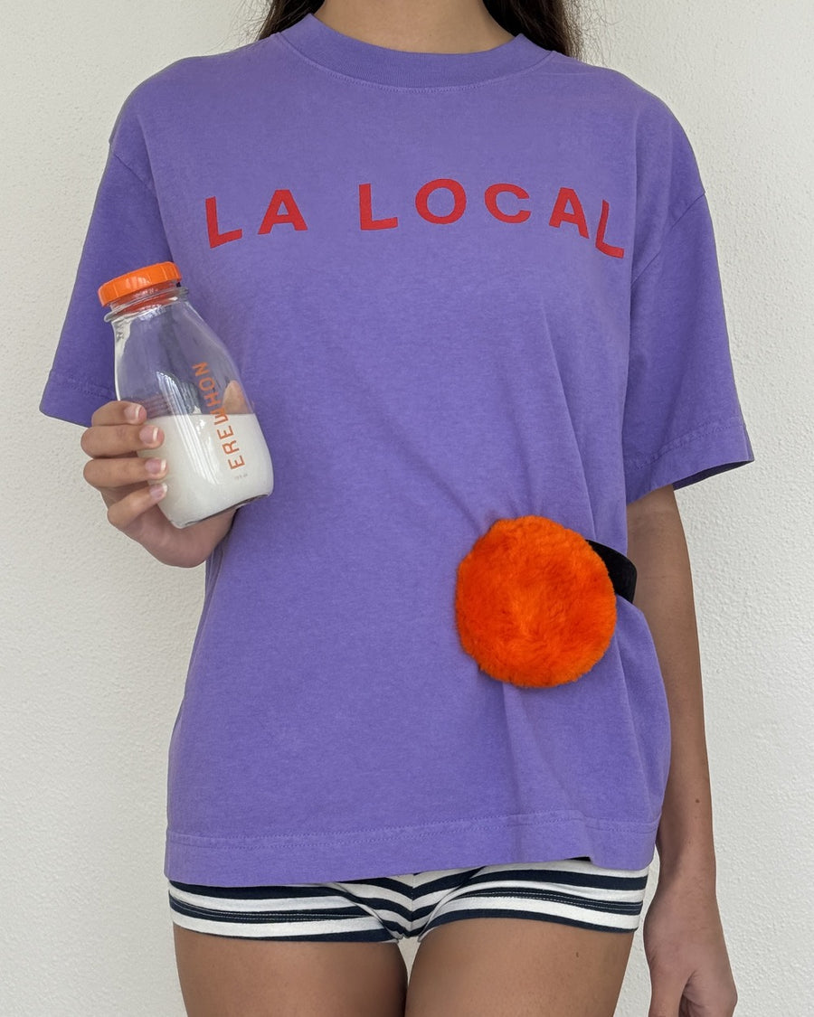Person in the purple LA LOCAL tee holding a milk bottle with an orange fuzzy pouch at the waist