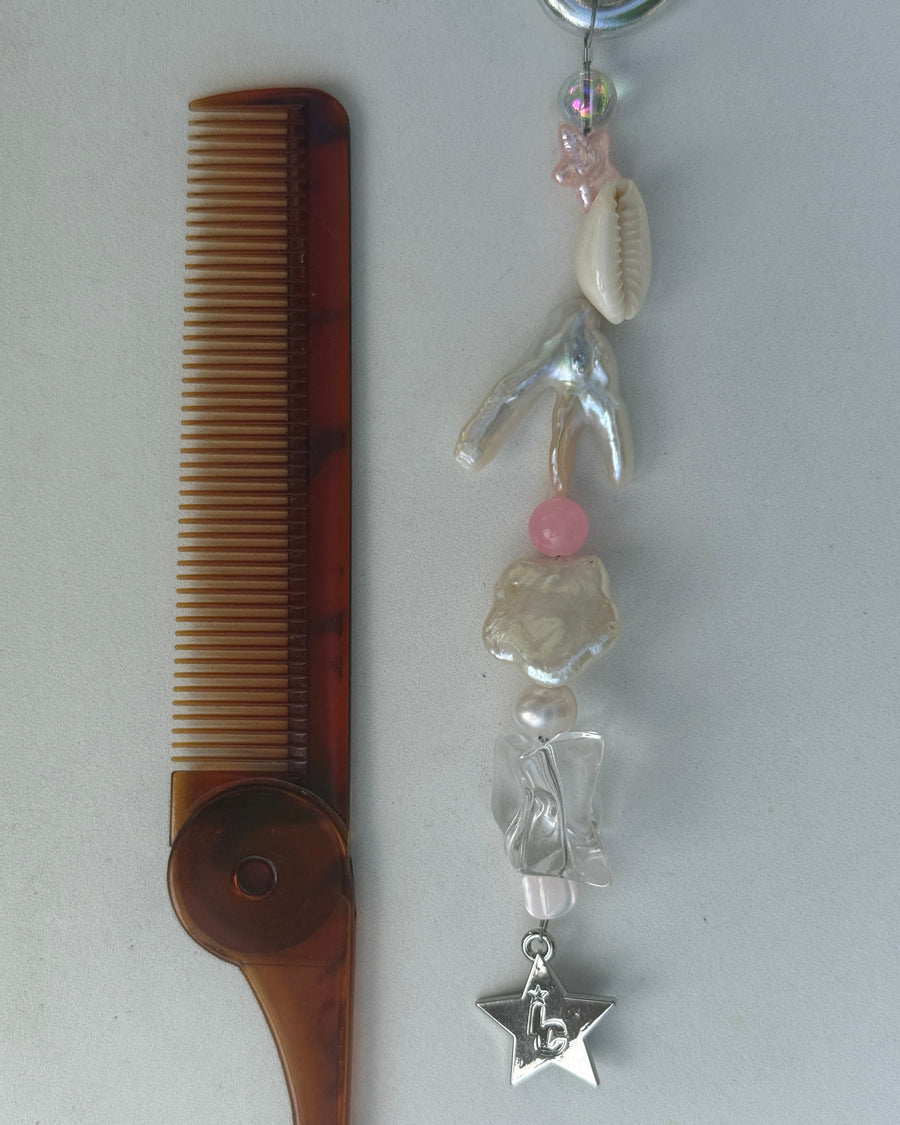 Marlee keychain with cowrie shells, coral, pink beads and a silver star charm beside a tortoiseshell comb