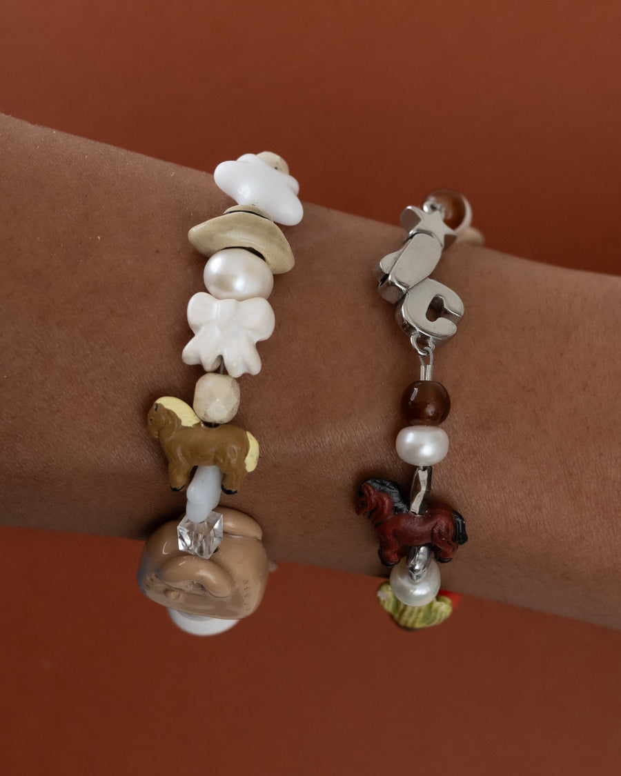 Close-up of a wrist stacked with quiet lux bracelets with pearl, flower and horse beads