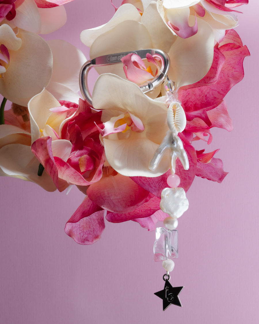 Marlee keychain with shells and a black star charm hanging among pink and white orchids