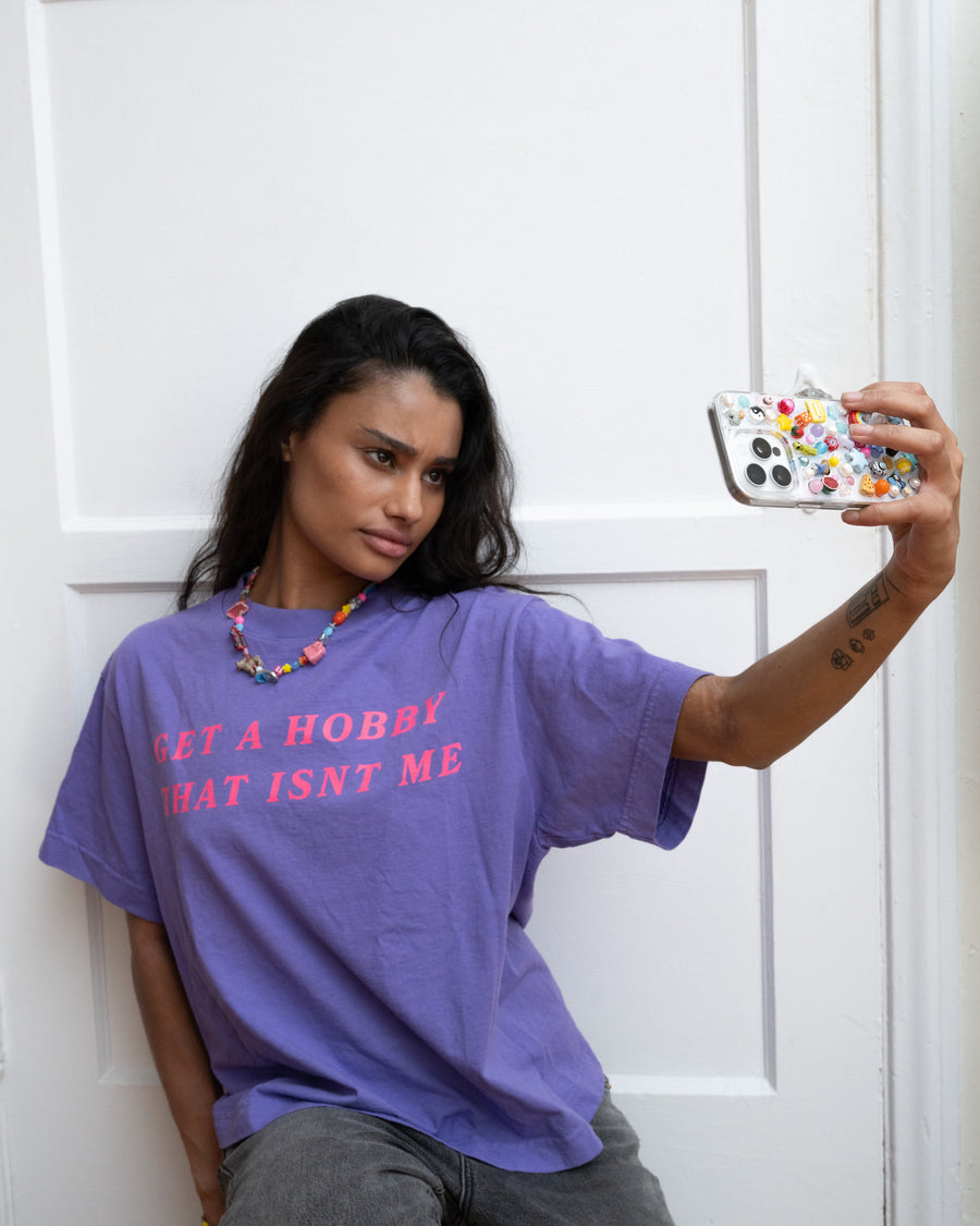 Woman in a purple slogan tee taking a mirror selfie with a colorful beaded charm phone case