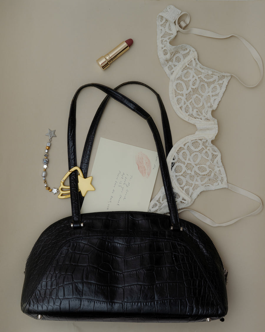 Black croc shoulder bag with the gold shooting star keychain, a red lipstick, a love letter and a white lace bra