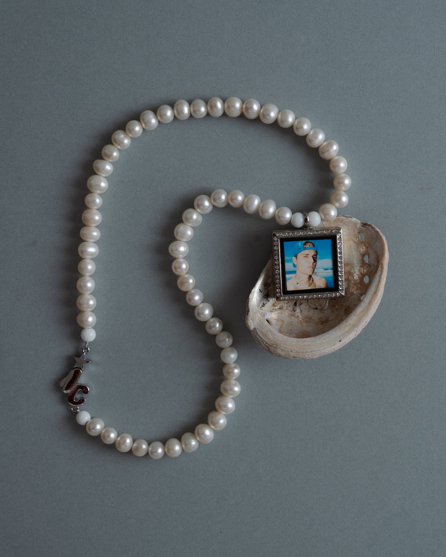 Custom pearl photo pendant necklace coiled around an abalone shell on a gray background