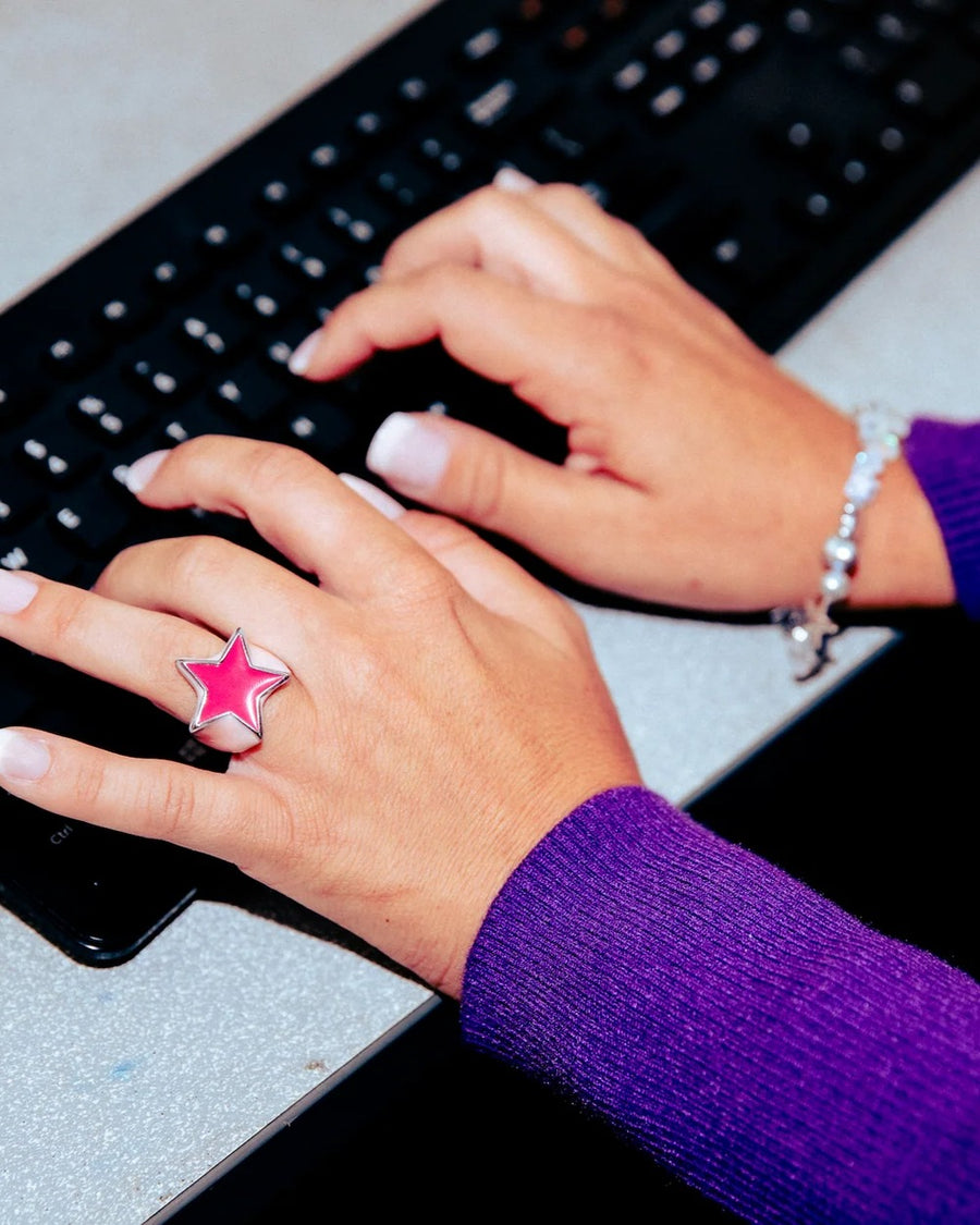 Hands typing on a keyboard wearing a pink enamel star ring and a beaded bracelet