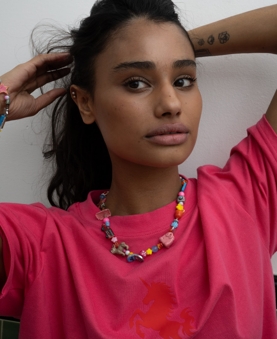 Woman in a pink tee with hands behind her head wearing the la necklace