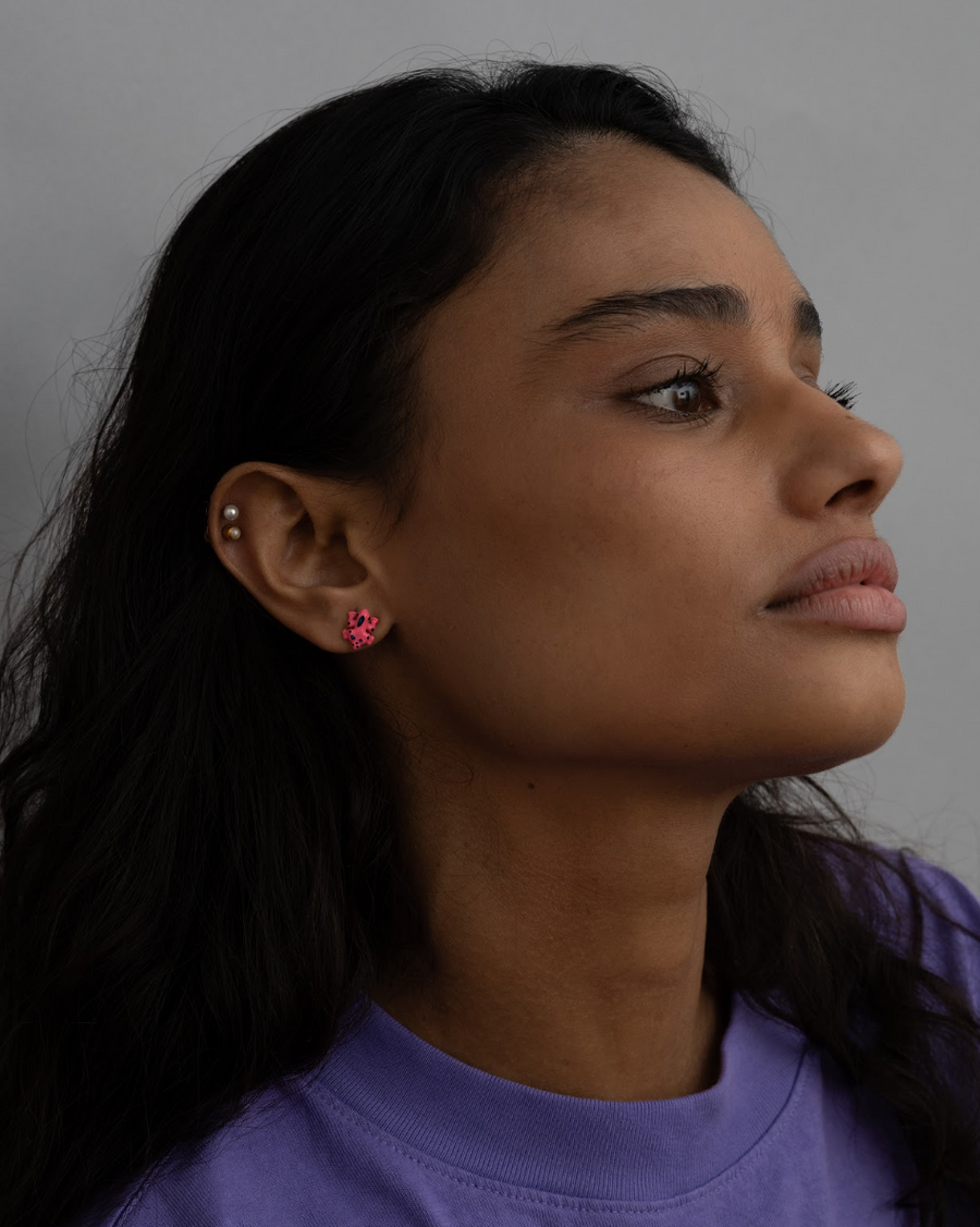 Profile of a woman with dark hair wearing a hot pink frog stud earring