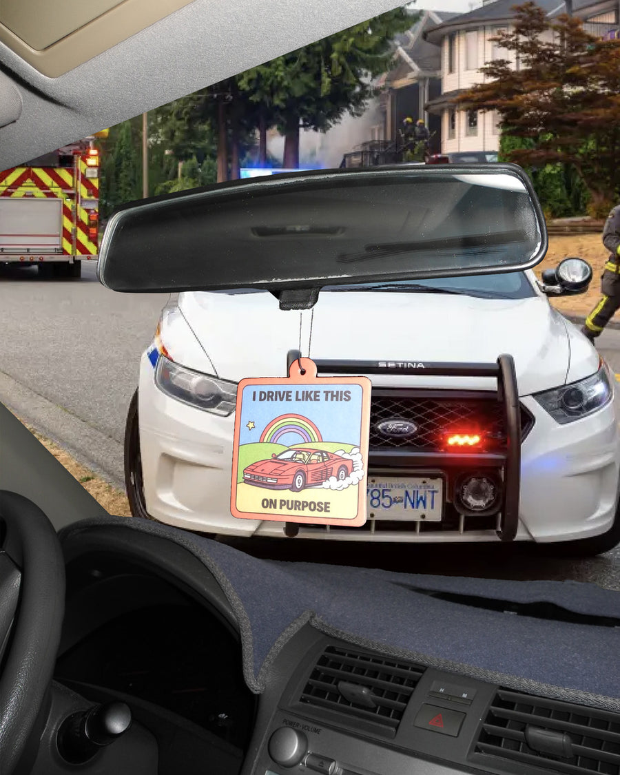 Worst driver air freshener hanging from a rearview mirror with a police car parked ahead