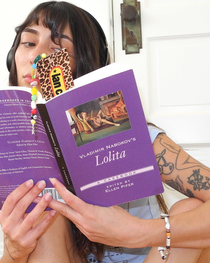 Woman reading a paperback novel with the leopard print ian charms beaded bookmark tucked in