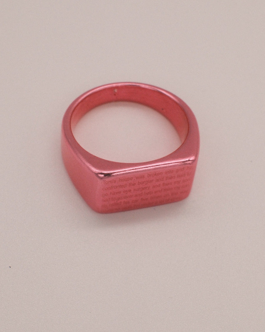 Metallic pink rectangular signet ring engraved with a block of tiny text – the break in ring