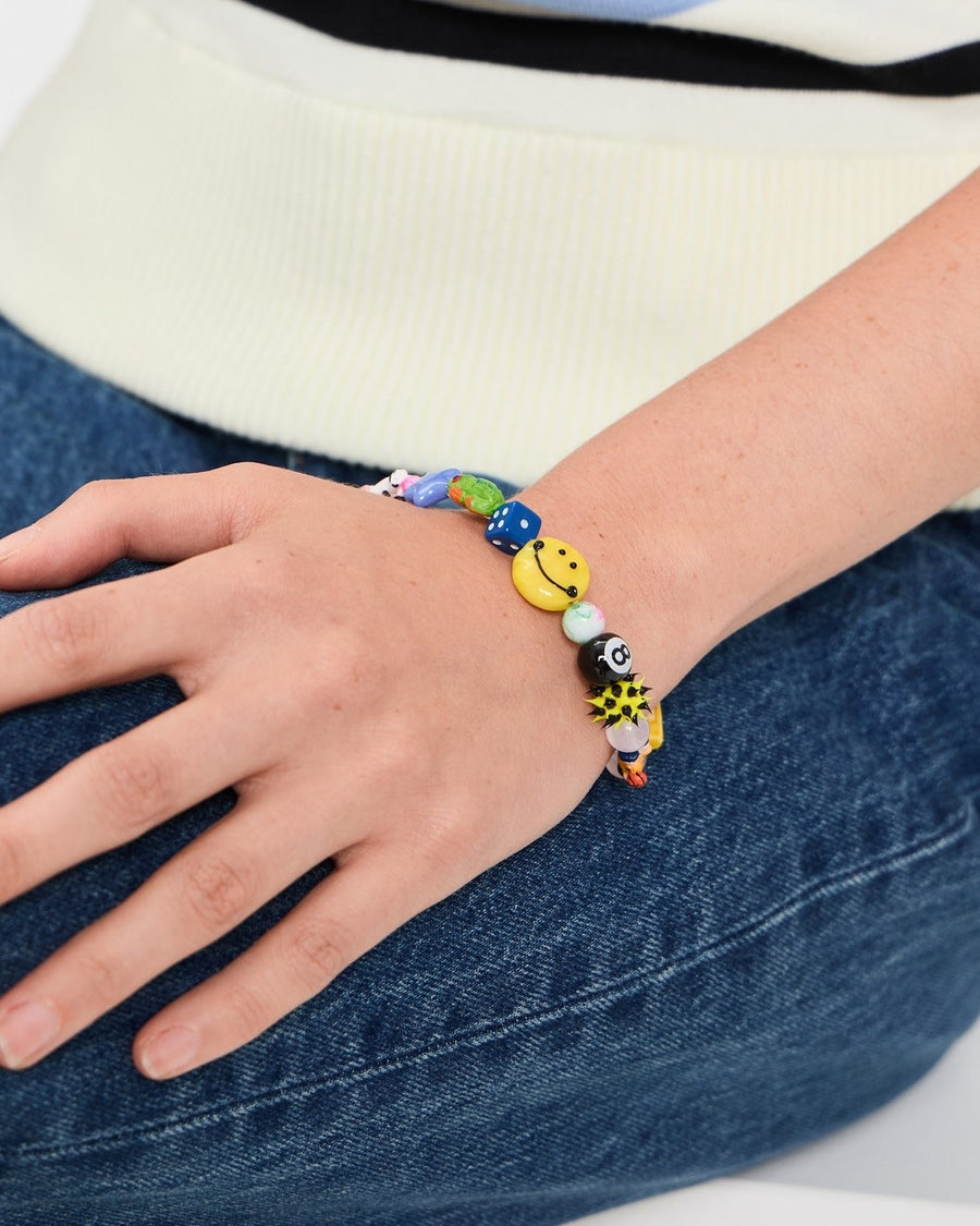 Wrist resting on jeans wearing a colorful beaded bracelet with a yellow smiley bead