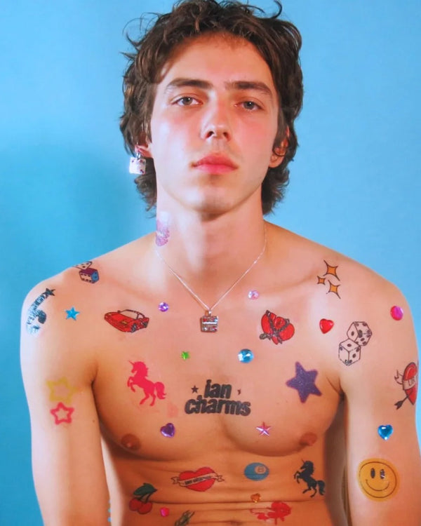 Shirtless man covered in colorful temporary tattoos wearing a silver rhinestone pendant necklace