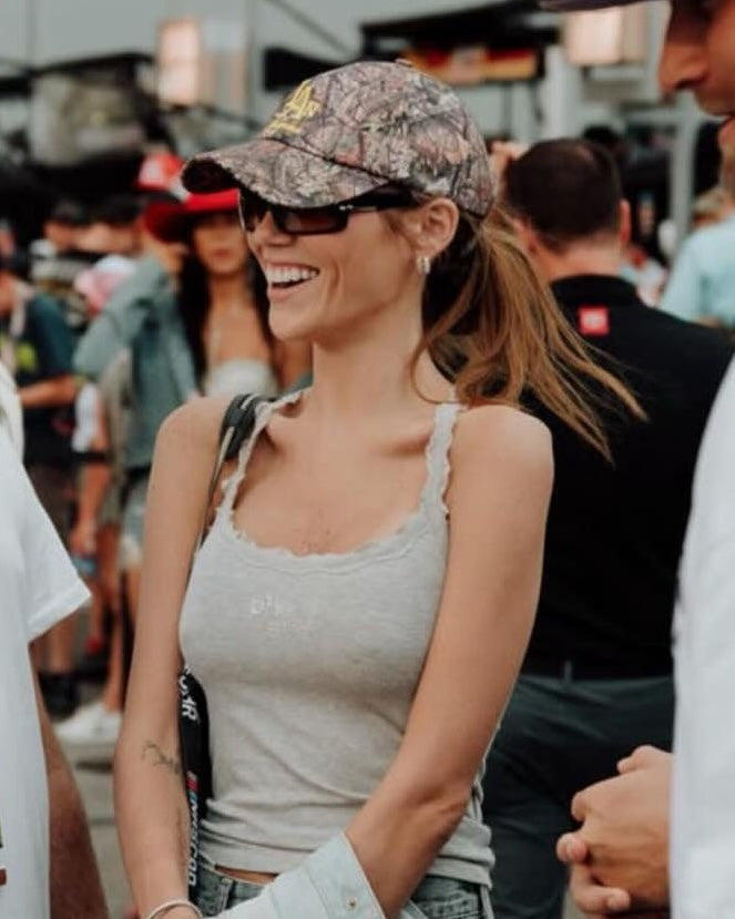Smiling woman in a crowd wearing the camo IC daddy cap and sunglasses