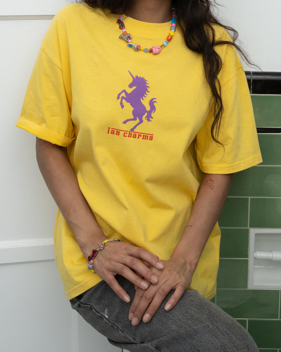 Seated woman in a yellow Ian Charms unicorn tee wearing the la necklace and LA bracelet