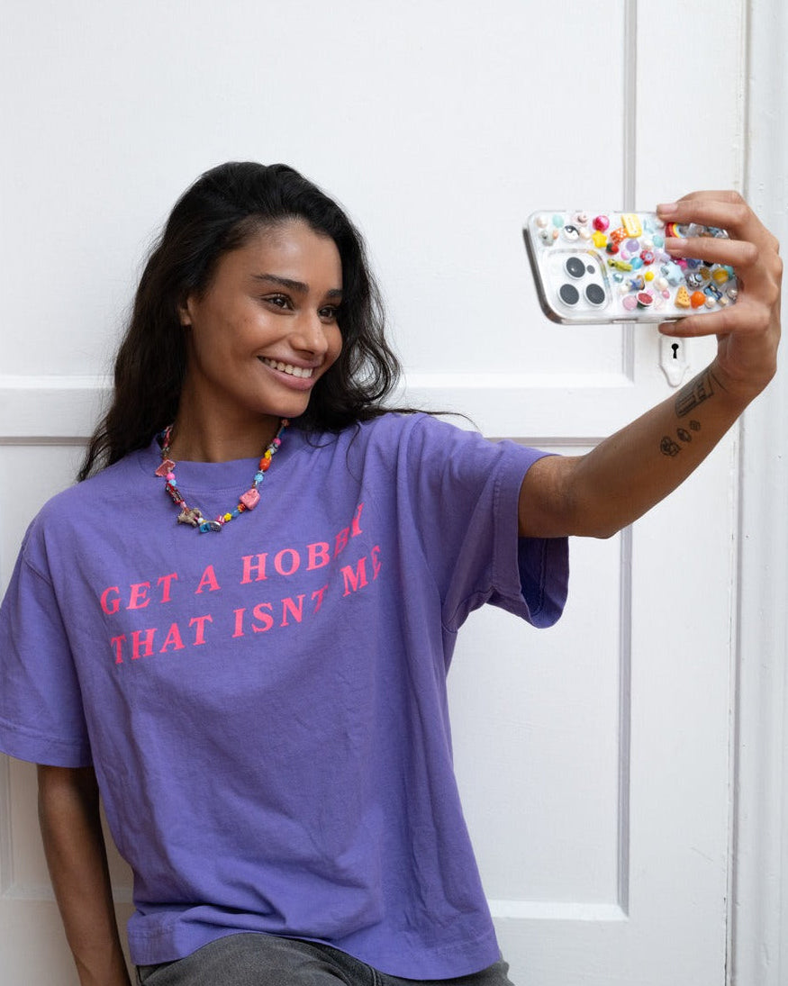 Woman in the purple get a hobby tee taking a selfie with the lisa phone case covered in colorful charms