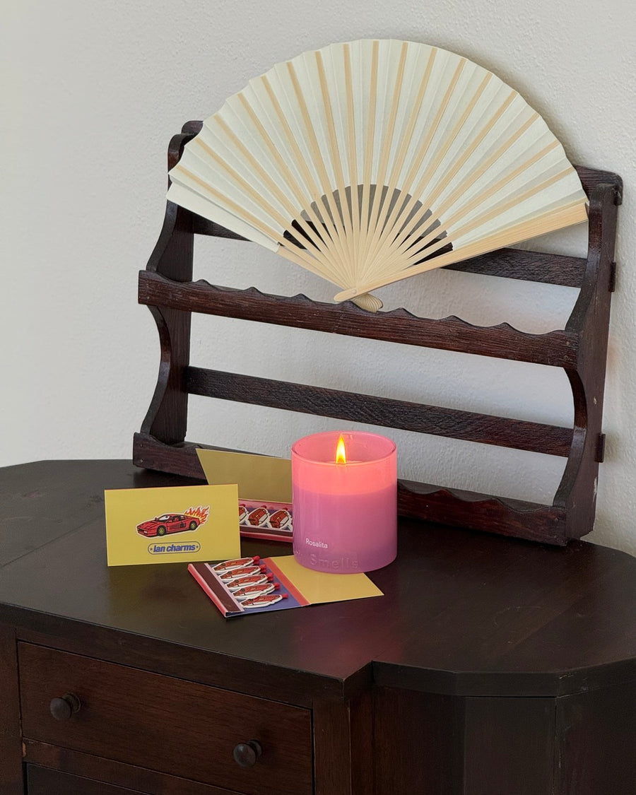 Michaels matchbook on a dark wood side table with a pink candle and a cream folding fan