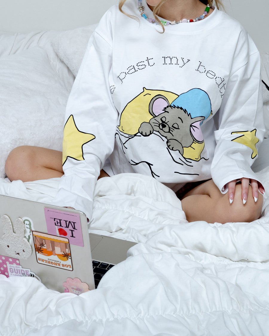 Woman sitting on a bed with a sticker-covered laptop wearing the oversized past my bedtime long sleeve