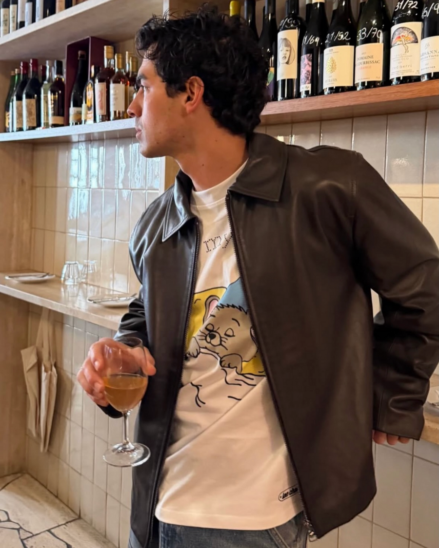 Man in a leather jacket at a wine bar wearing the past my bedtime long sleeve tee