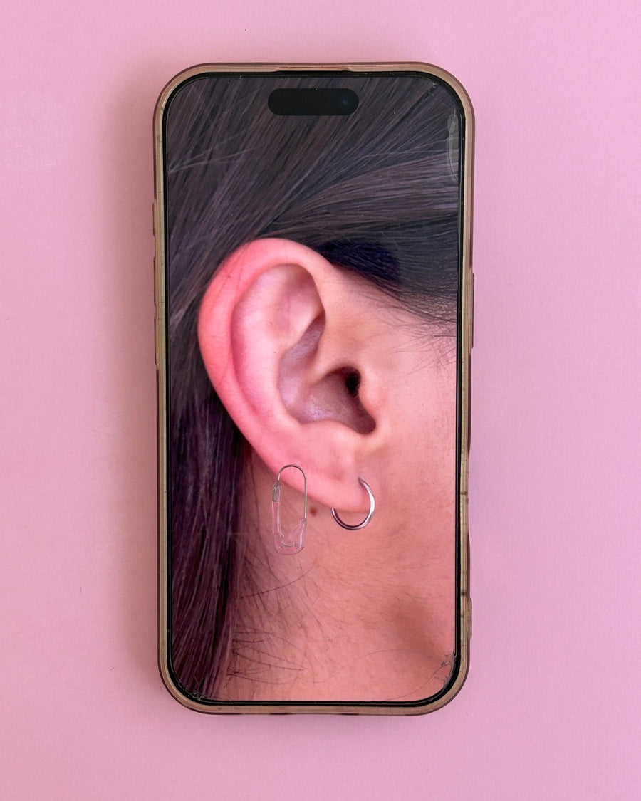 Phone screen on pink showing an ear wearing a clear resin safety pin earring