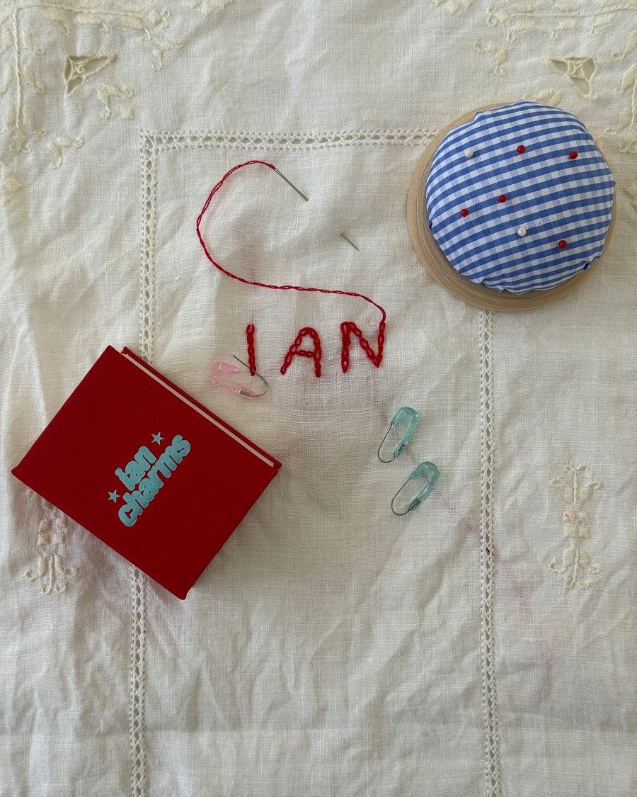 Safety second earrings on embroidered linen next to a red Ian Charms box and a gingham pincushion