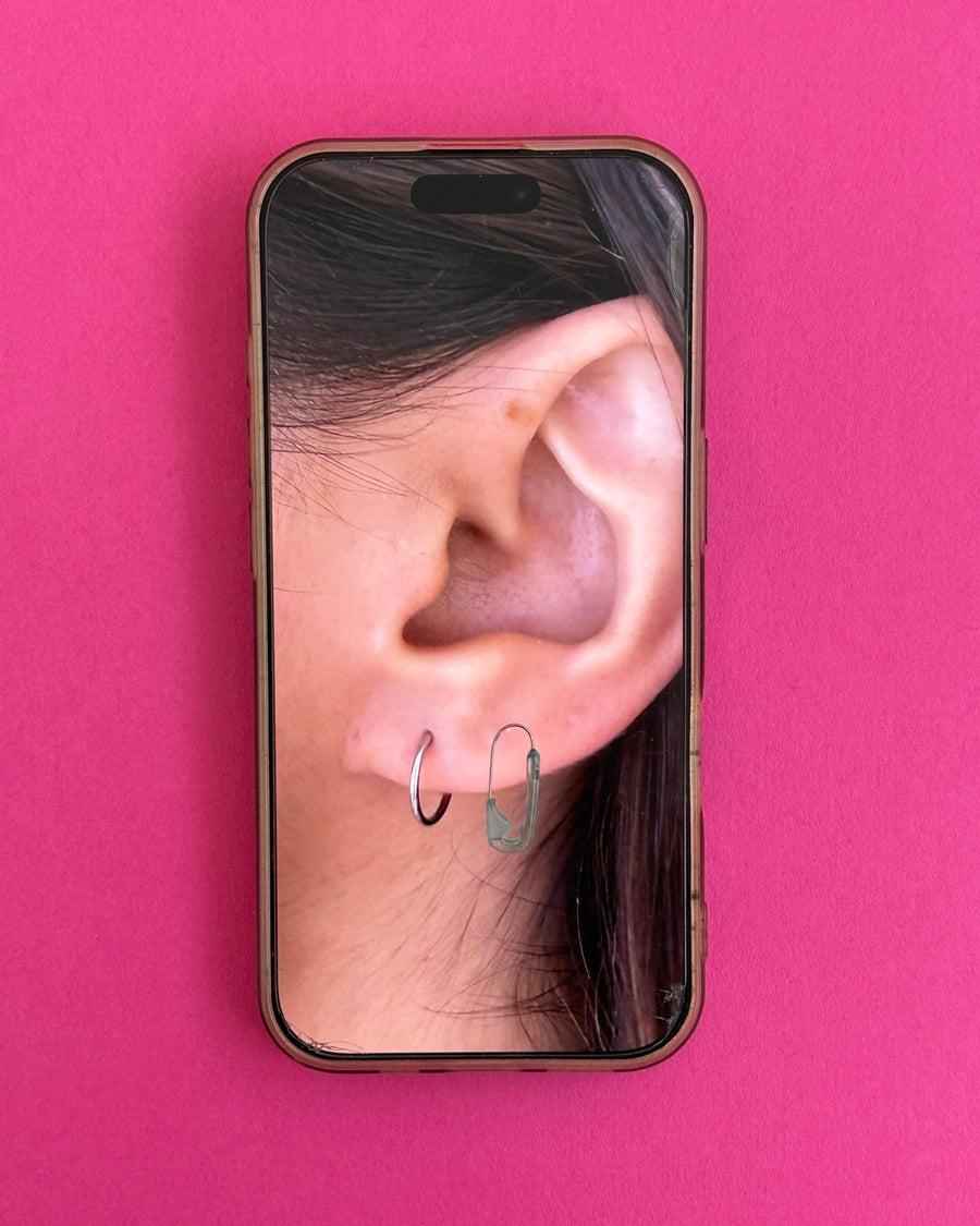 Phone screen on hot pink showing an ear wearing a clear resin safety pin earring