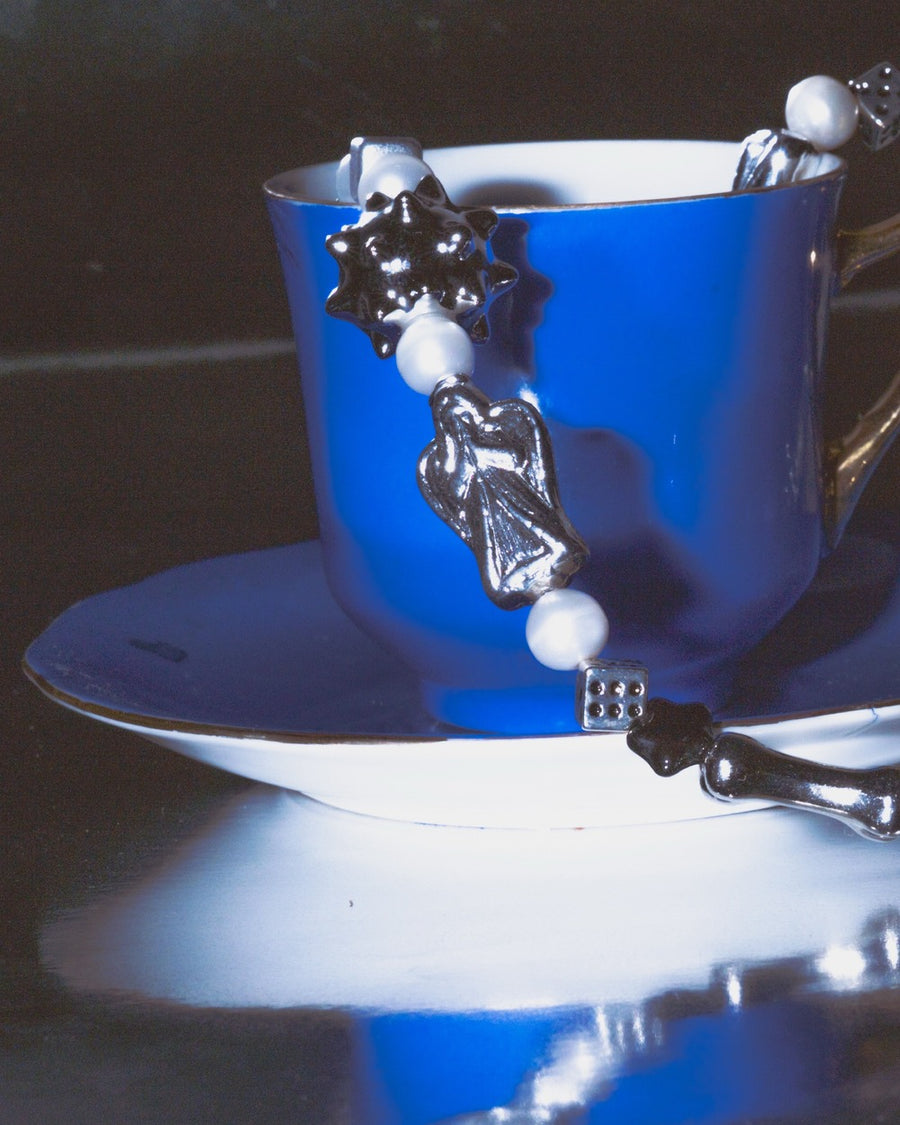The sloane necklace with silver spiky and heart beads draped on a cobalt blue teacup