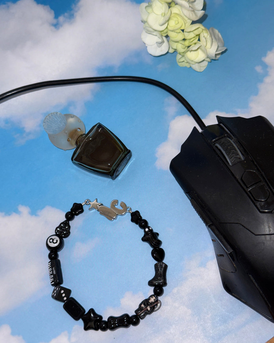 The smoker black beaded bracelet styled on a cloud backdrop with a computer mouse and perfume bottle