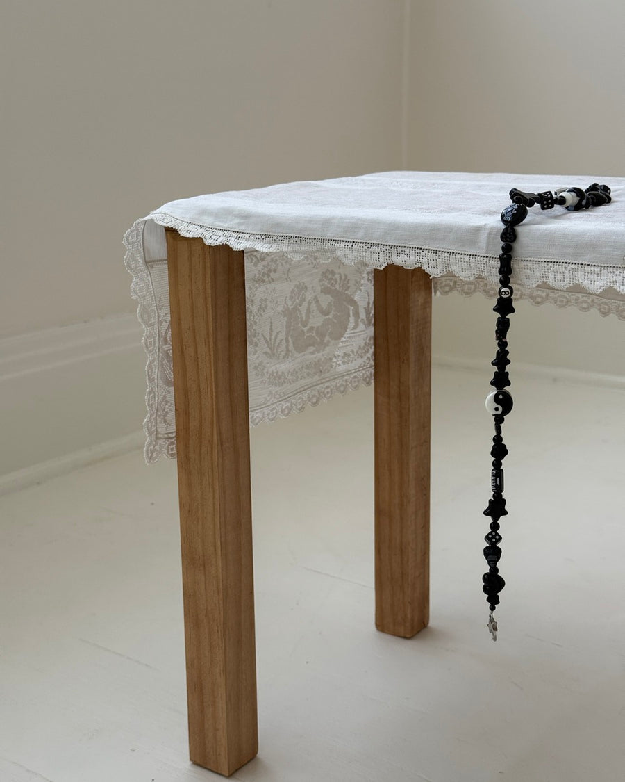 The smoker black beaded necklace hanging from a wooden table with a white lace tablecloth